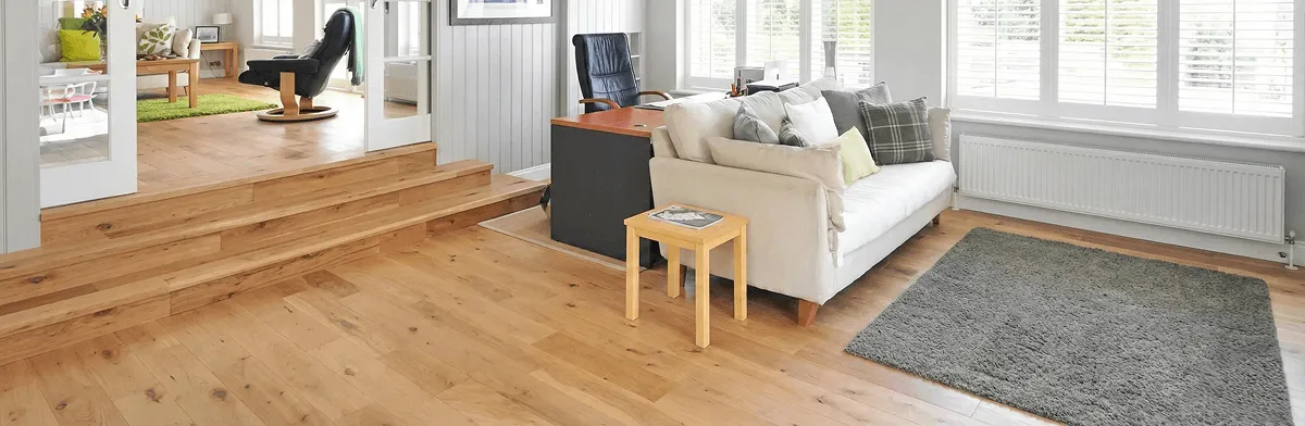 A modern living room with professionally installed laminate flooring, a beige sofa, a small side table, a gray rug, and large windows with white shutters in Atlanta, GA